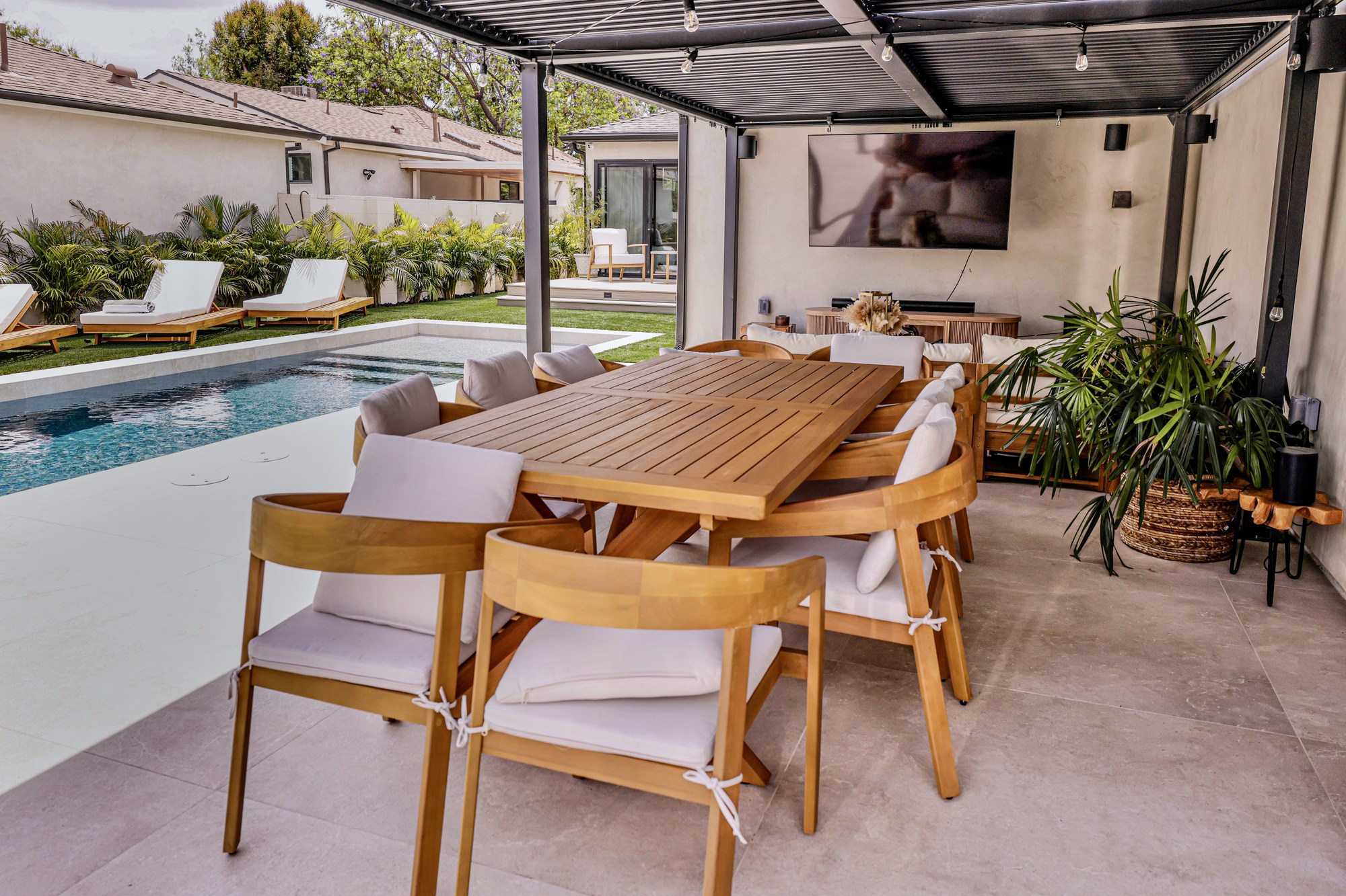 Covered outdoor room with a louvered pergola and dining beside the pool